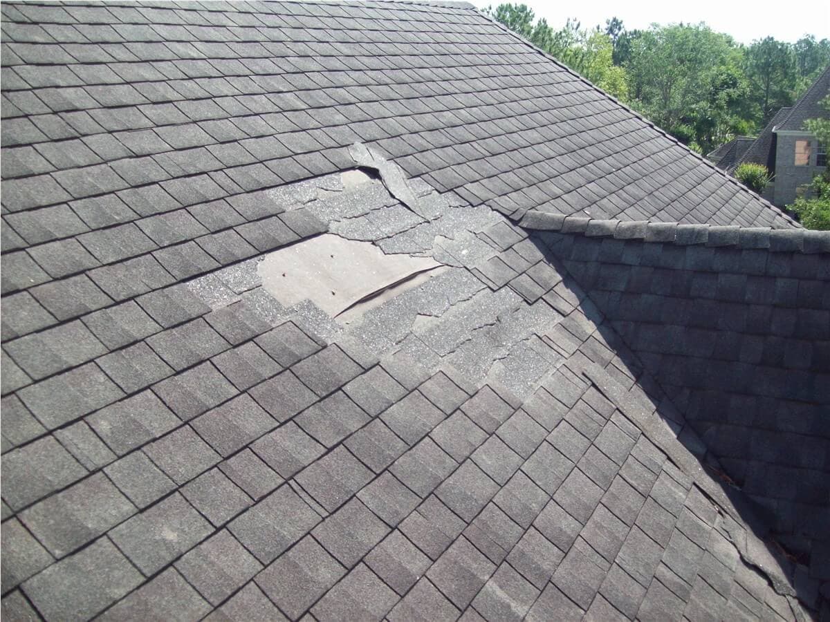 Damaged asphalt shingles opened to expose a roof repair area